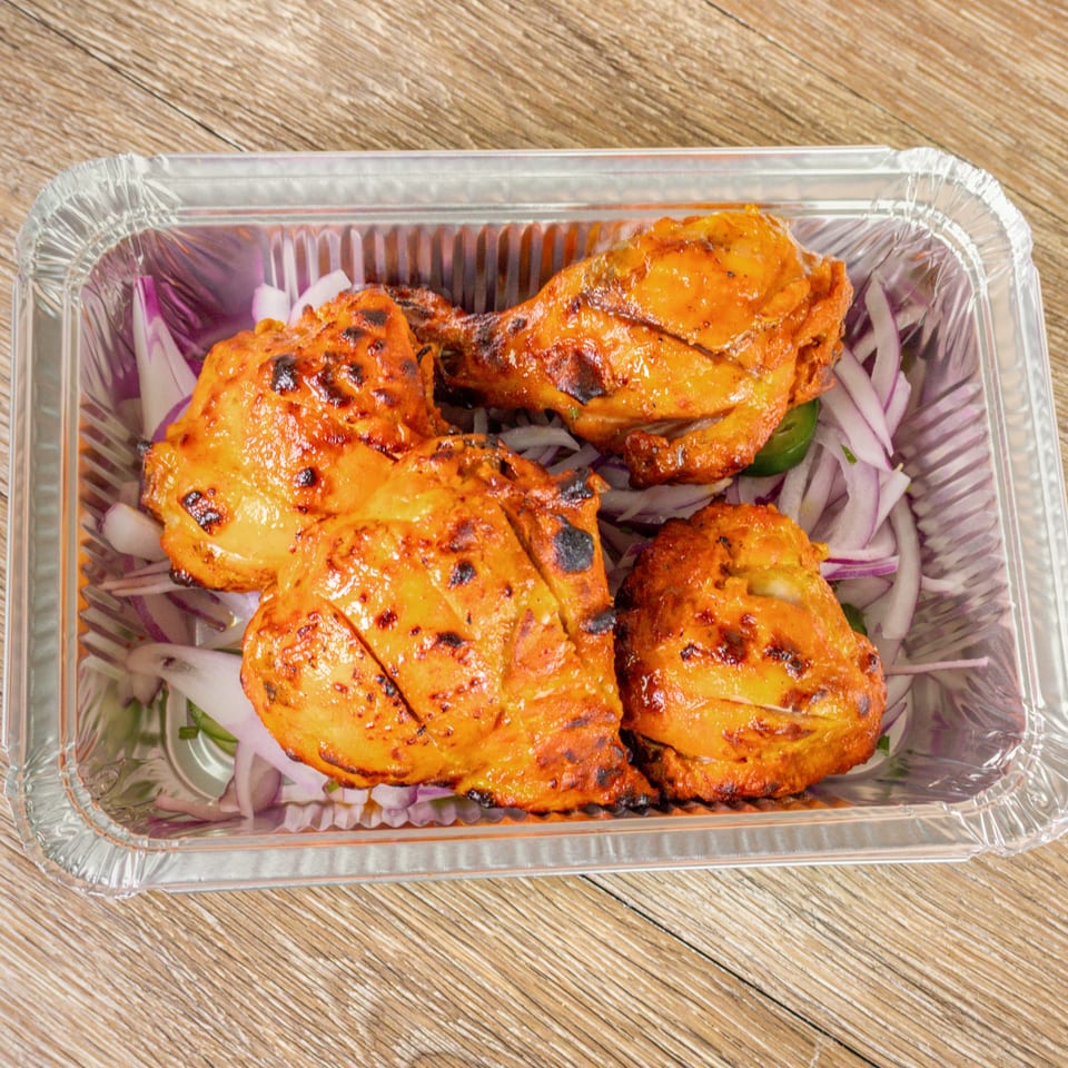 Grilled orange-marinated chicken pieces served with sliced red onions and green peppers in a foil tray.