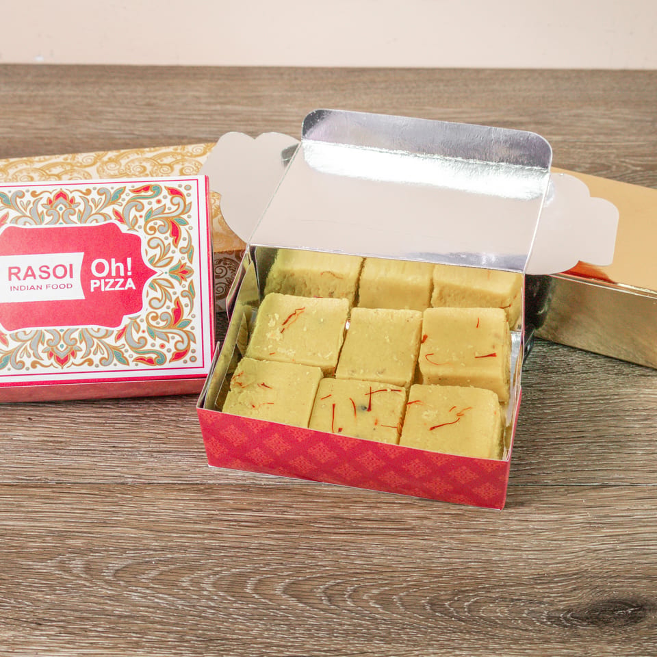 Open boxes of saffron-topped Indian sweets beside ornate Rasoi Oh! Pizza packaging on a wooden table.