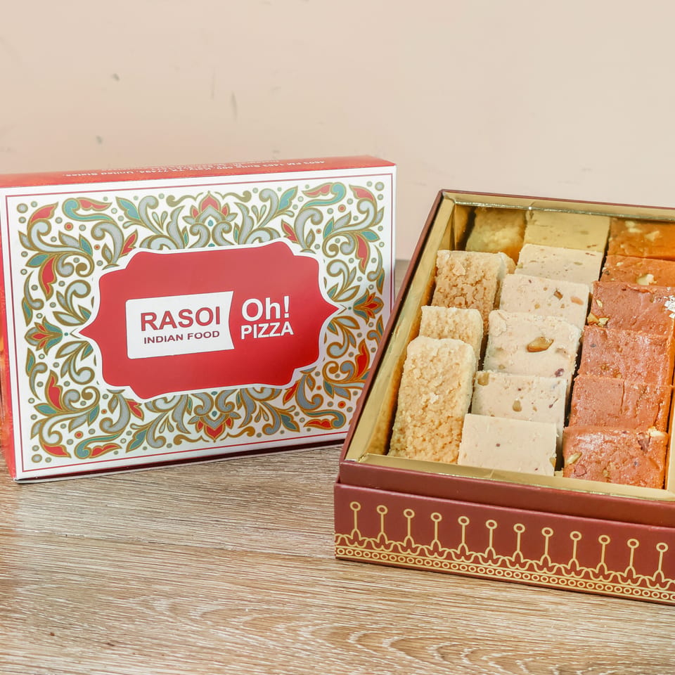Assorted Indian sweets arranged in an ornate Rasoi Oh! Pizza gift box on a wooden table.